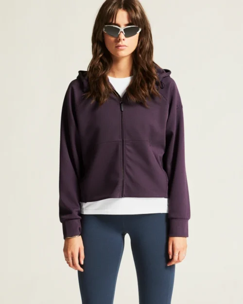 Nainen poseeraa luumunvärinen vetoketjullinen huppari päällä